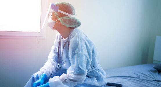 A doctor in PPE sits on a bed to rest.