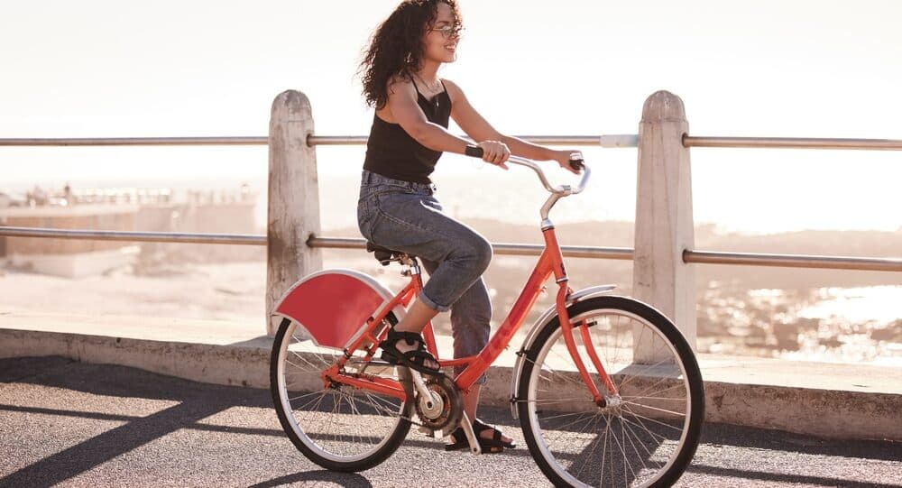 Woman, cycling and bike at beach for travel with freedom, sea and sunshine with eco friendly journey in Los Angeles. Bicycle, exercise and adventure by the coast, carbon footprint and sustainability