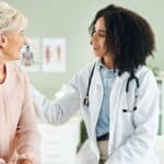 Senior,Woman,,Doctor,And,Comfort,In,Consultation,With,Discussion,,Smile